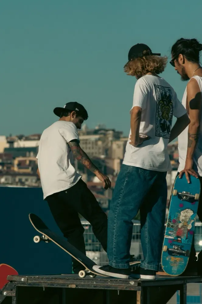Três amigos skatistas de camiseta no topo de uma rampa com a cidade ao fundo