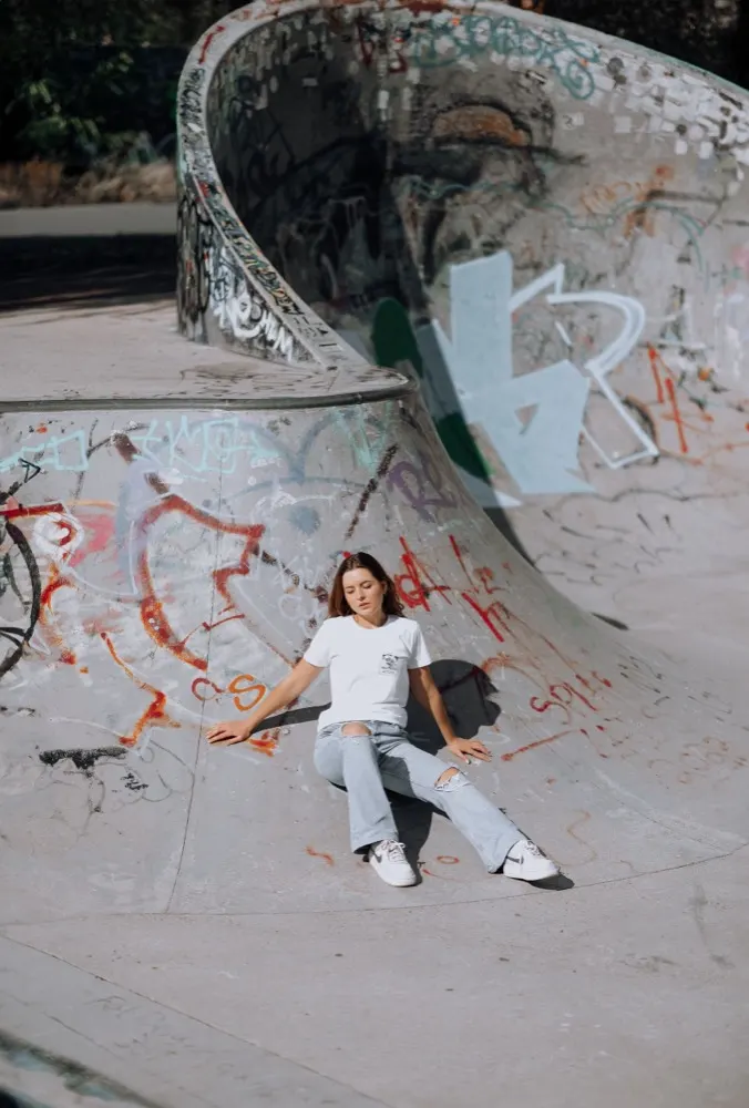 Jovem de camiseta branca sentada em bowl de skatepark colorido com graffiti