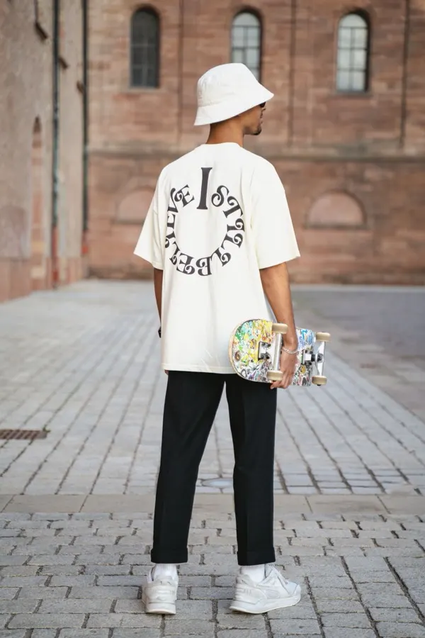 Camiseta oversized off-white com estampa circular nas costas usada com bucket hat em calçada de pedra