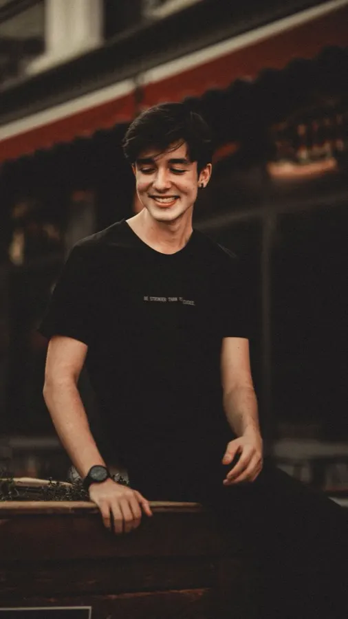 Jovem sorrindo vestindo camiseta oversized preta lisa em rua urbana ao entardecer