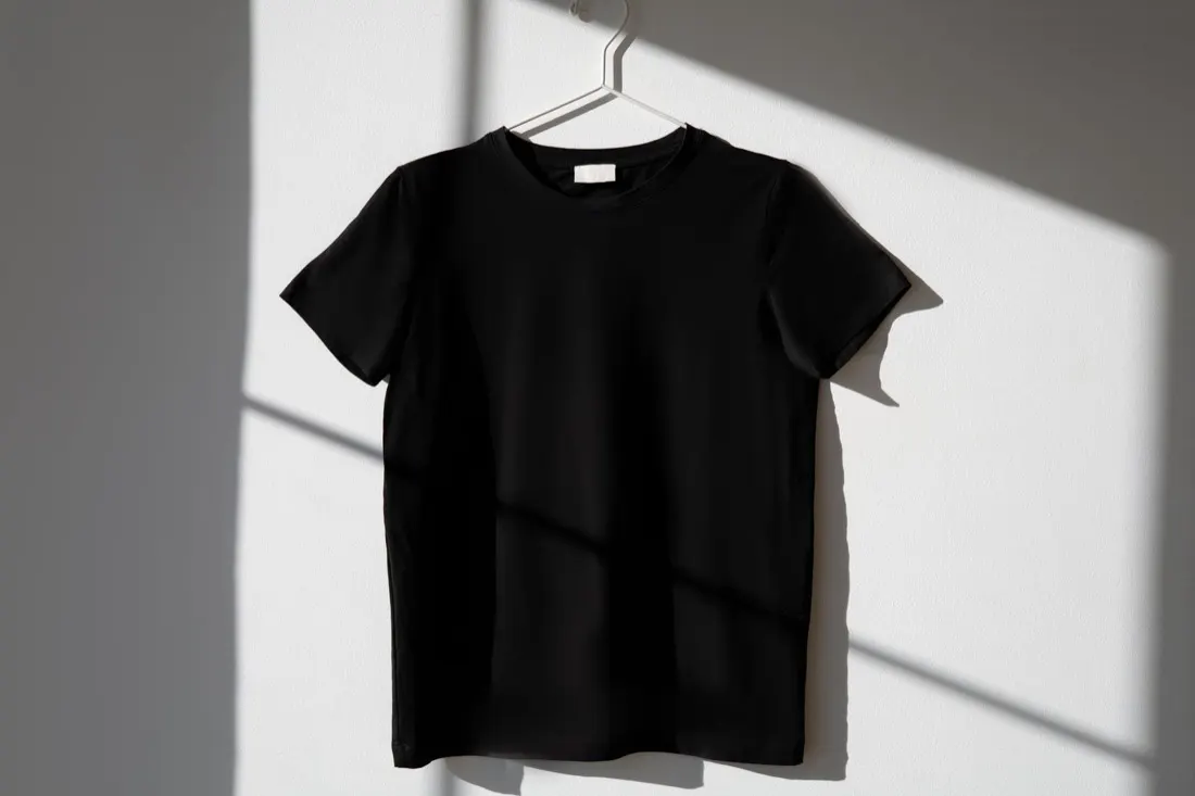 Camiseta preta lisa de algodão pendurada em cabide branco com luz e sombra de janela