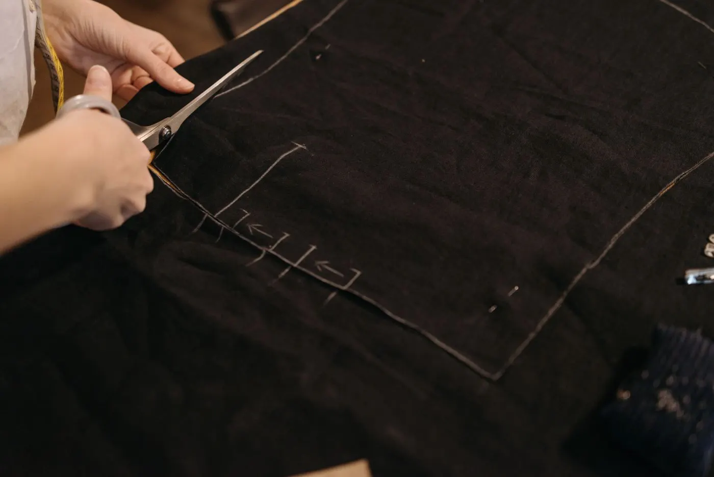 Mãos cortando tecido preto sobre a mesa de corte da fábrica seguindo a marcação do molde