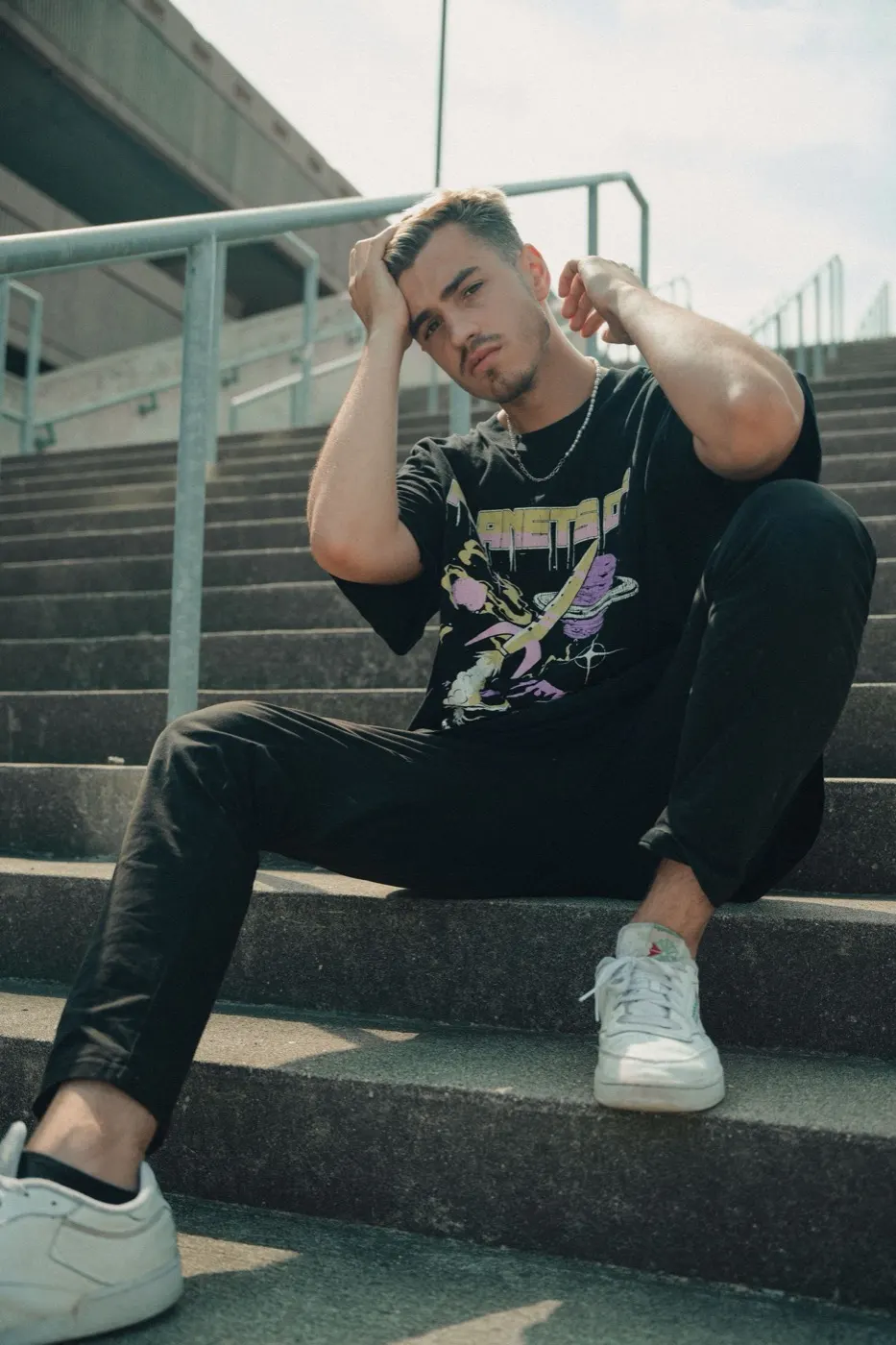 Jovem sentado em escadaria urbana de concreto vestindo camiseta oversized preta com estampa colorida moderna
